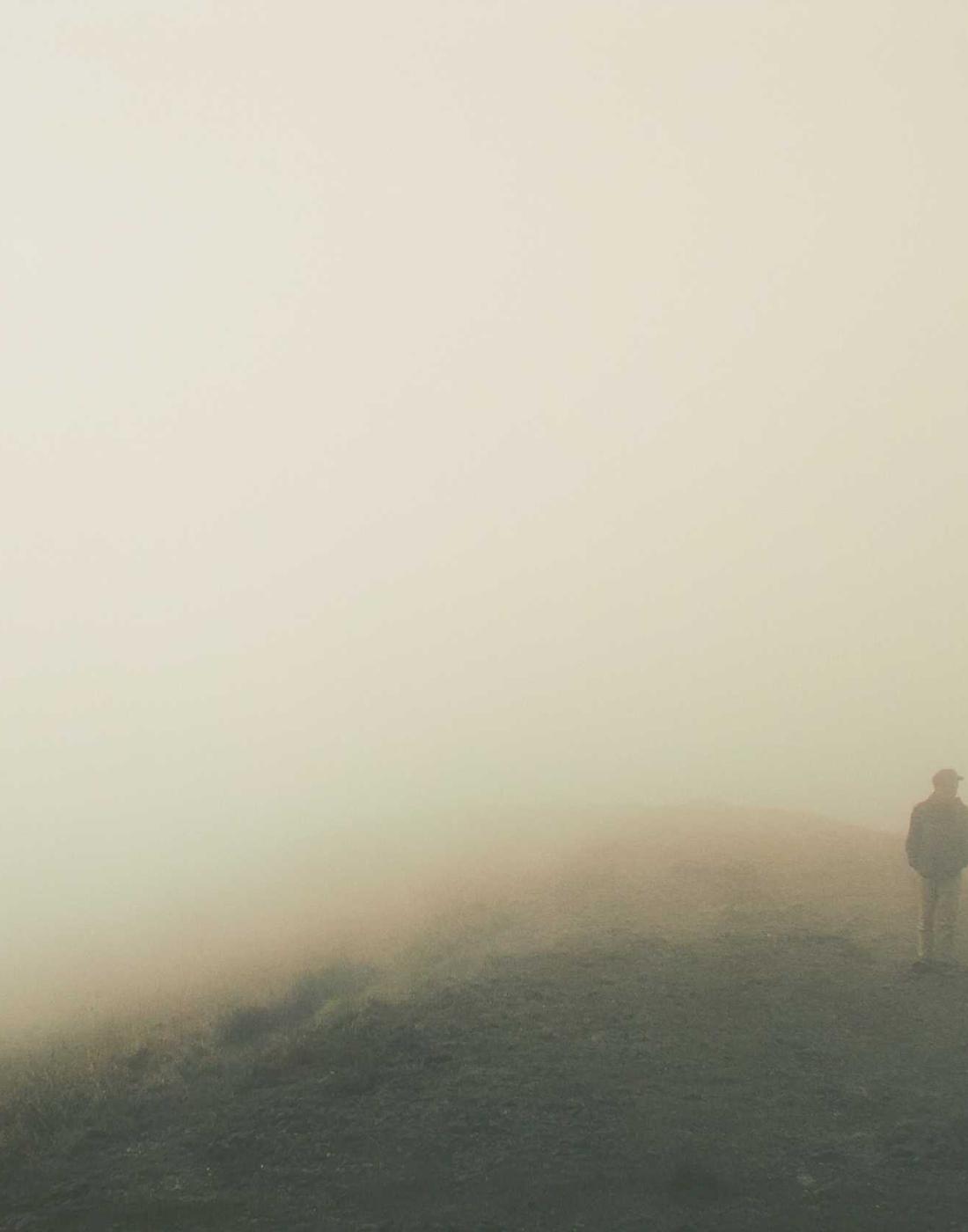 A lone figure standing on a fog-covered ridge